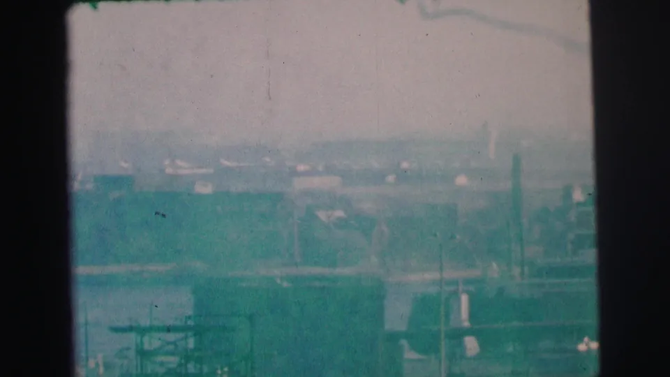 1973 Lynbrook, New York 8mm frame with a soft, blue-green view of shoreline buildings, water, and distant industrial forms.