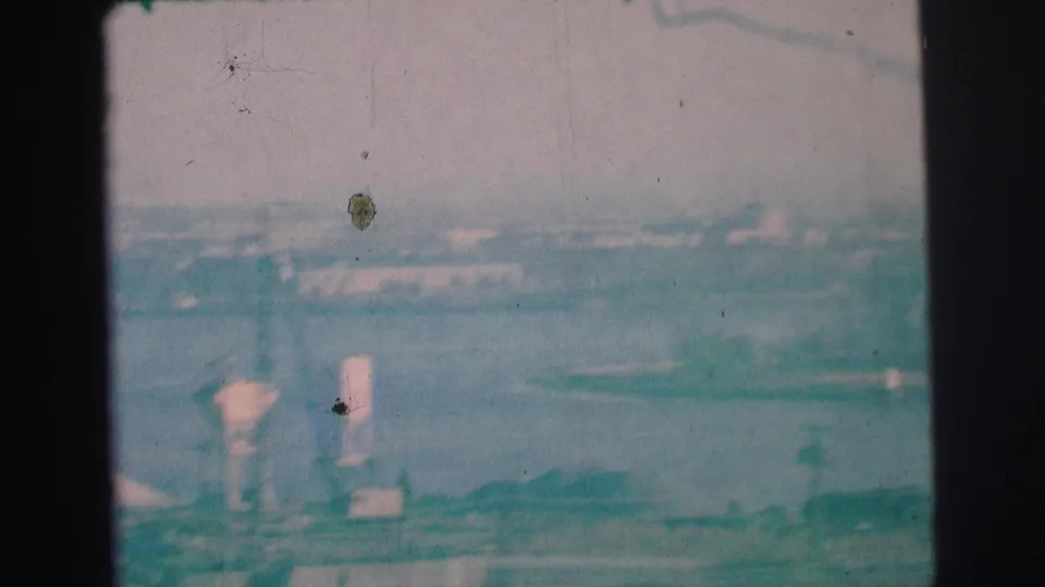 1973 8mm frame from Lynbrook, New York, showing a soft hazy harbor view with distant industrial shoreline features and visible film wear.
