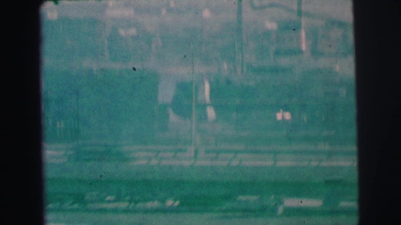 Soft green-blue elevated view of buildings and street edges through dark film borders.