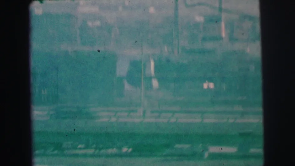 Grainy 1973 Lynbrook, New York home-movie frame showing a hazy elevated view of buildings, poles, and street edges.