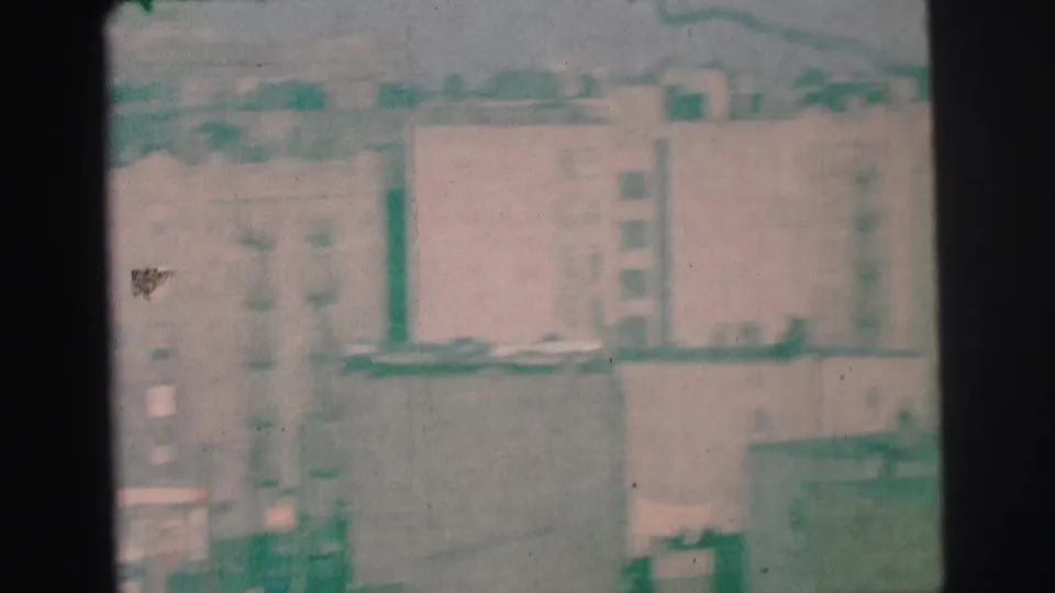Grainy 1973 Lynbrook frame of mid-rise apartment facades, fire escapes, rooftops, and nearby street details.