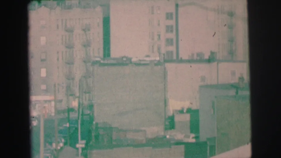 Grainy 1973 Lynbrook view of apartment buildings, rooftop edges, utility poles, and small parked cars below.