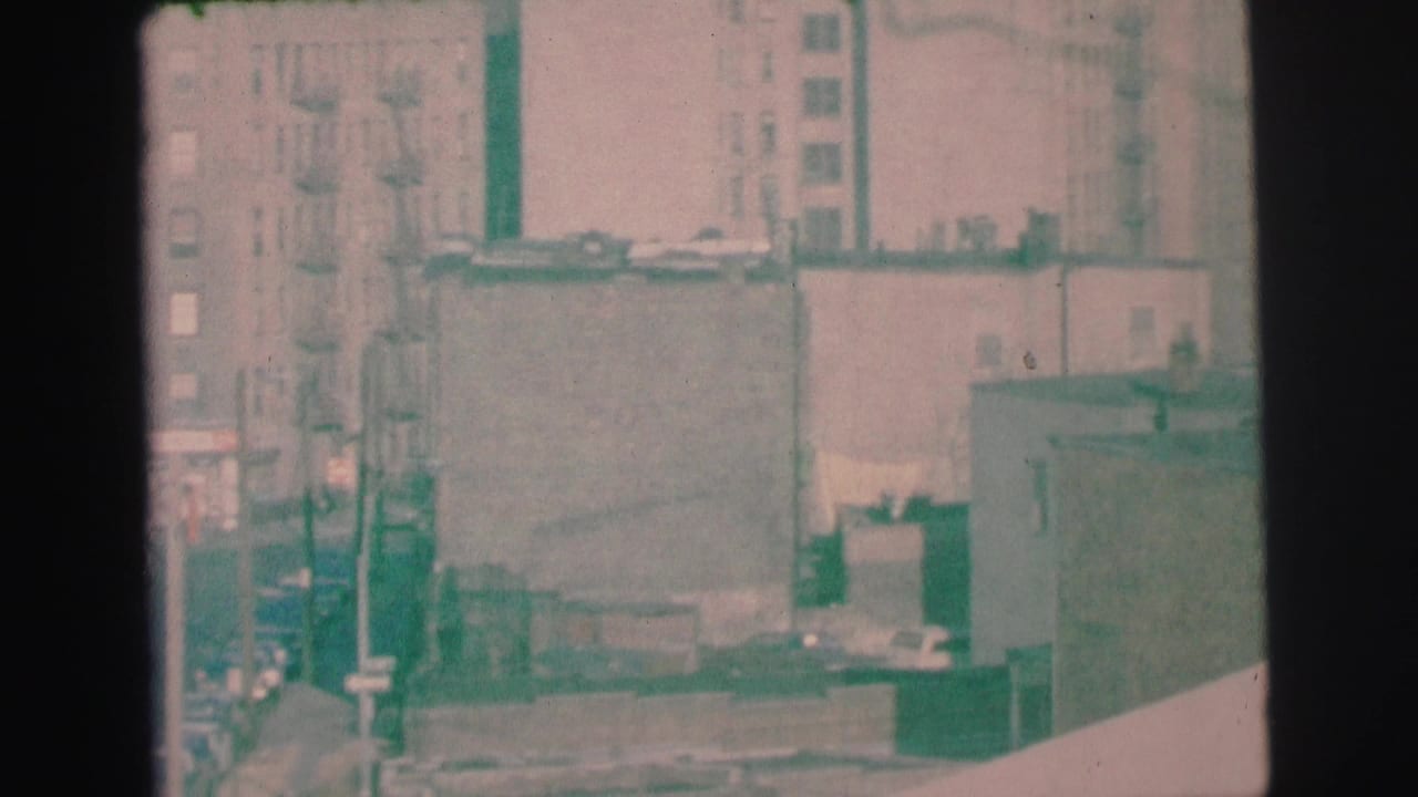 1973 Lynbrook, New York home-movie frame showing hazy commercial buildings, fire escapes, and rooftops from a high vantage point.
