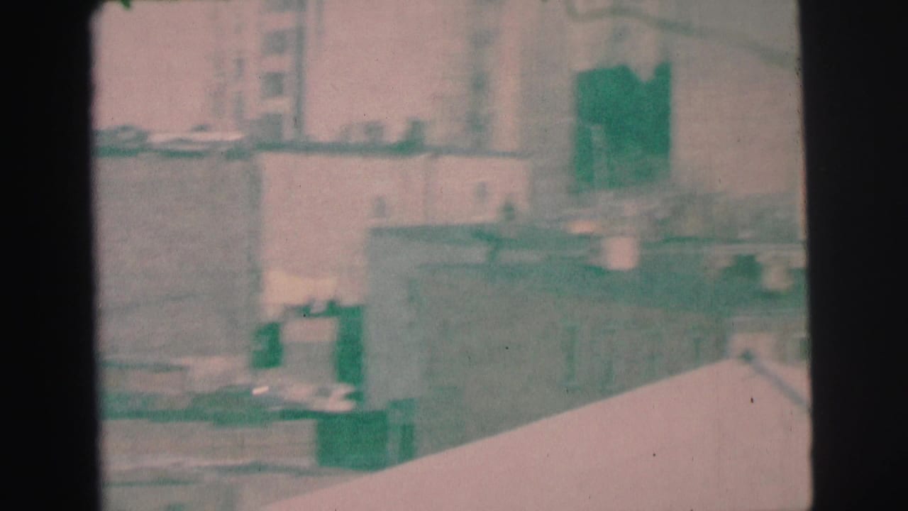 1973 Lynbrook, New York frame with blurred rooftops, building walls, and a pale foreground roof under greenish haze.