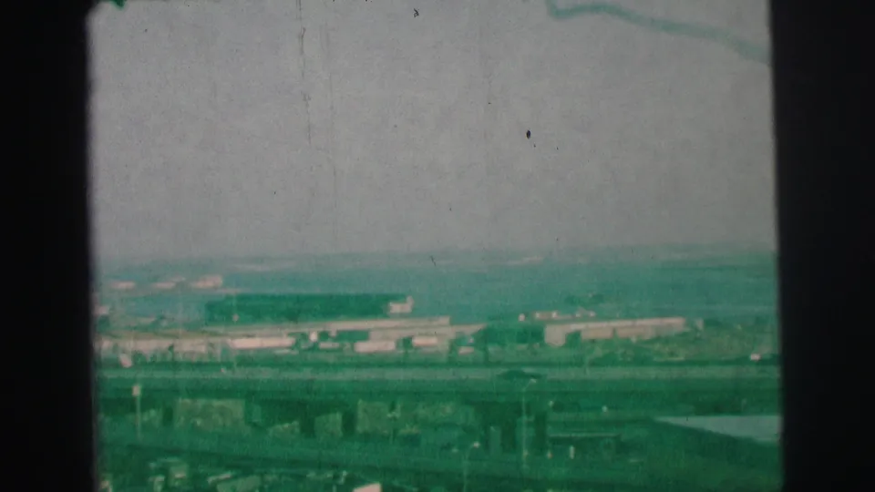 1973 Lynbrook, New York frame with elevated view over highways, low commercial structures, and a soft distant skyline.