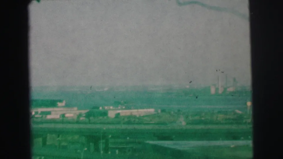 1973 Lynbrook, New York 8mm frame showing roads, low buildings, distant industrial stacks, and visible film grain.