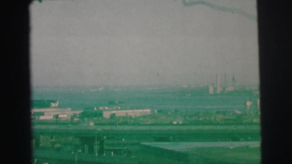 1973 Lynbrook, New York 8mm frame showing a hazy elevated roadway view with distant industrial buildings and smokestacks.