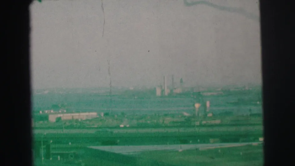 1973 Lynbrook, New York 8mm frame showing a hazy elevated view across traffic lanes toward industrial smokestacks in the distance.