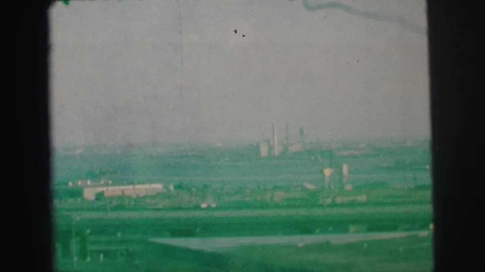 1973 Lynbrook-area home-movie frame showing a green-tinted elevated view over highways, cars, low buildings, and distant smokestacks.