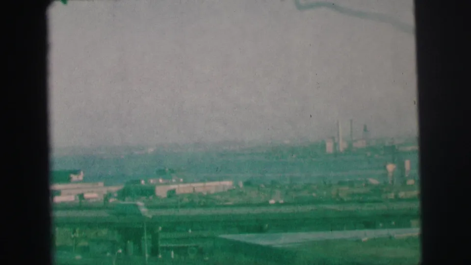 Green-tinted 1973 Lynbrook-area frame with traffic below, layered motorway structures, industrial buildings, and a hazy horizon.