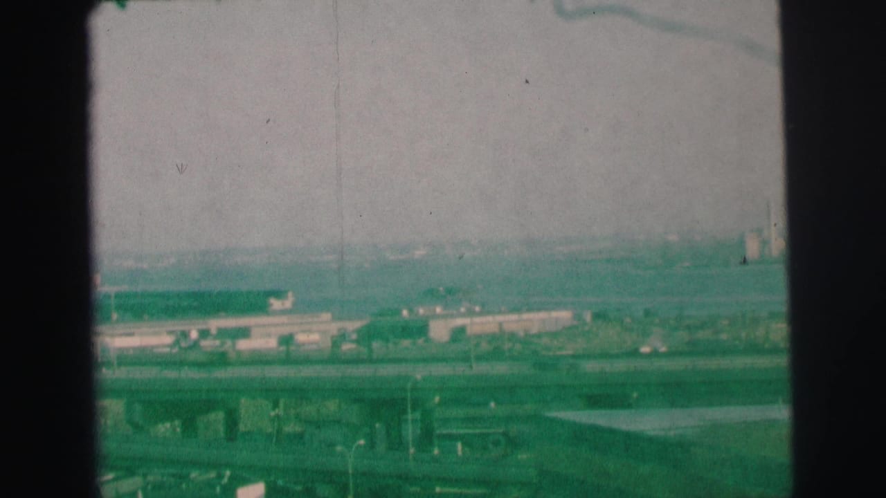 Hazy elevated view of bridges, low buildings, and distant industrial landscape under a gray sky.