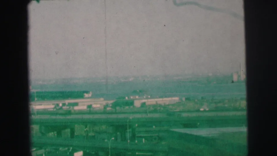 1973 Lynbrook, New York 8mm frame showing a green-tinted elevated view of bridges, overpasses, low structures, and distant haze.