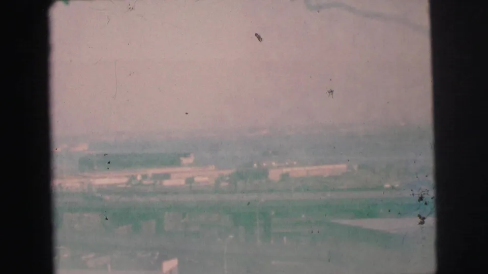 Faded green-pink 8mm frame from 1973 Lynbrook, New York with a hazy industrial view, overpasses, and visible dust and scratches.