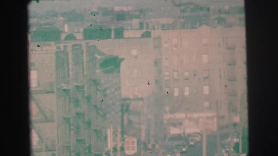Faded 1973 Lynbrook city view with brick apartment blocks, exterior fire escapes, rooftops, and parked cars along the street.