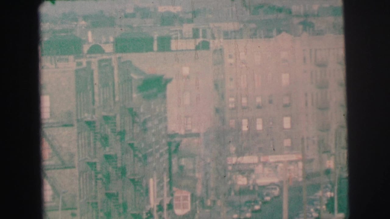 Distant apartment buildings with exterior fire escapes and parked cars below.