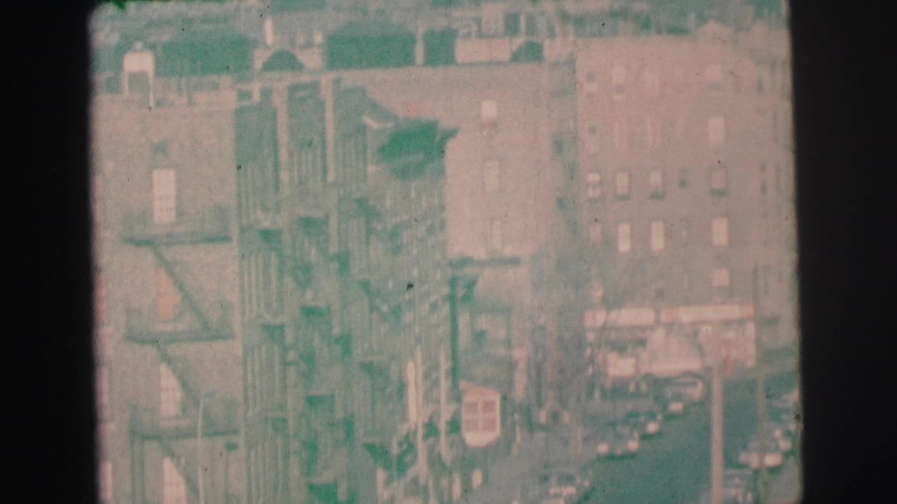 Apartment building facades with fire escapes and cars along the street.