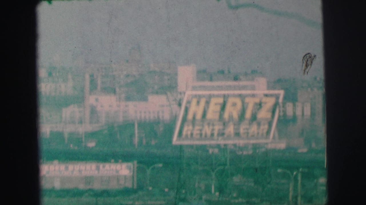 Distant Hertz Rent-A-Car sign above a hazy commercial streetscape.