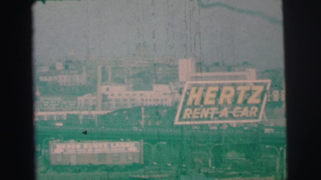 Distant Lynbrook commercial view with prominent Hertz branding and a bowling-lanes sign below.