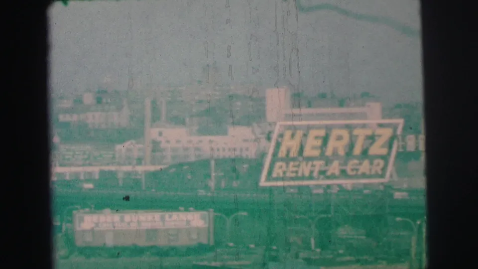 Distant Lynbrook commercial view with prominent Hertz branding and a bowling-lanes sign below.