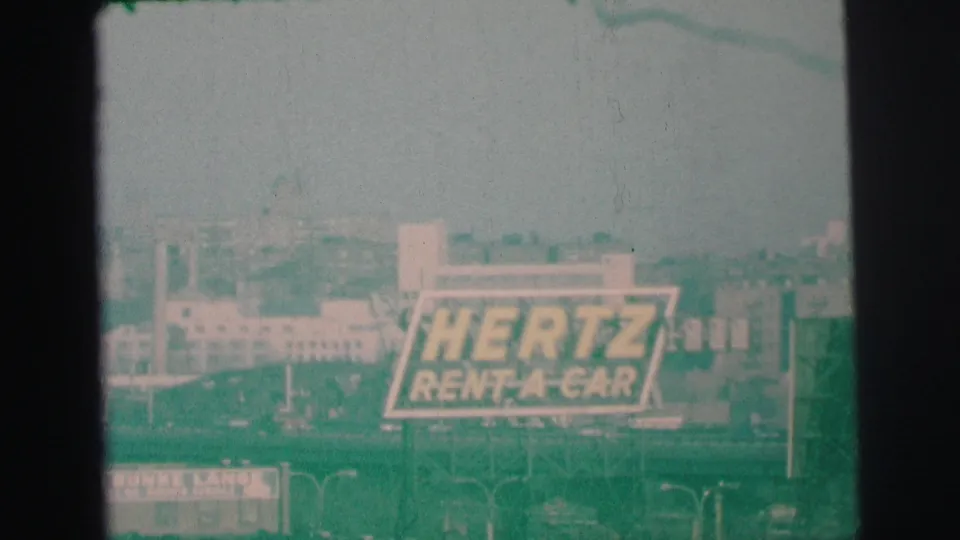 1973 Lynbrook, New York frame with the Hertz Rent-A-Car sign centered against a hazy commercial backdrop.