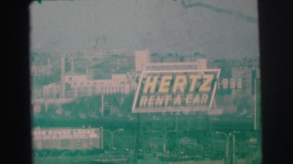 The Hertz billboard remains centered over a Lynbrook streetscape, with soft focus, grain, and visible film edges.