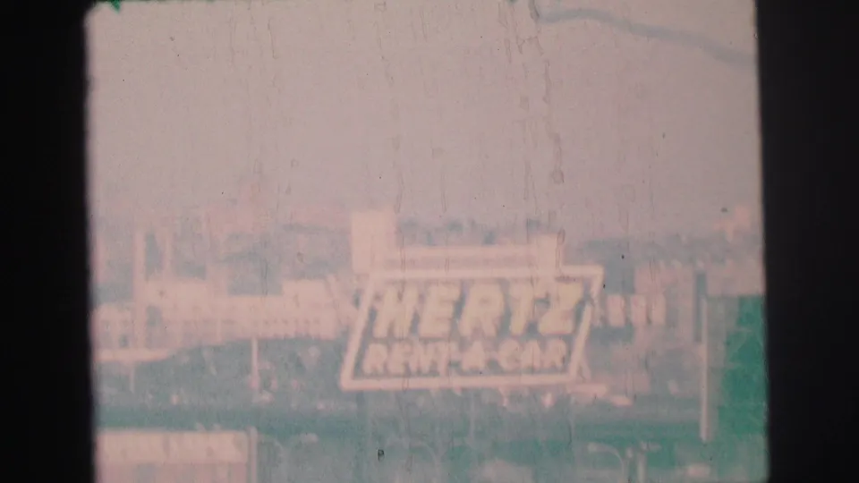 Soft, pale 1973 8mm frame with the Hertz Rent-A-Car sign partially washed by exposure and film wear.