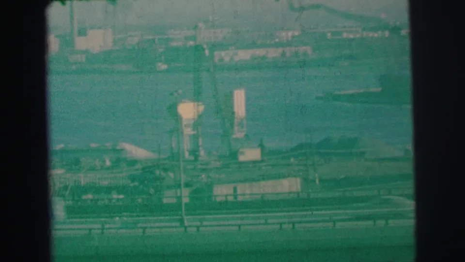 1973 Lynbrook, New York view of cars on a freeway below bay water and distant industrial structures across the shoreline.