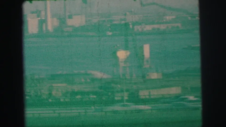 1973 Lynbrook, New York 8mm frame with highway lanes, small vehicles, bay water, and shoreline industrial forms in soft focus.