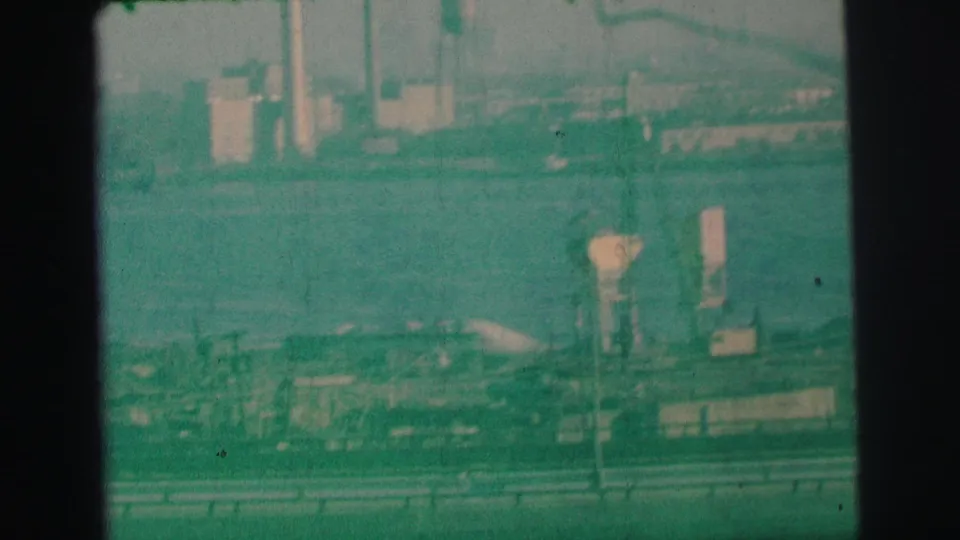 1973 Lynbrook, New York closing frame showing freeway traffic, guardrails, bay water, and distant industrial shoreline equipment.