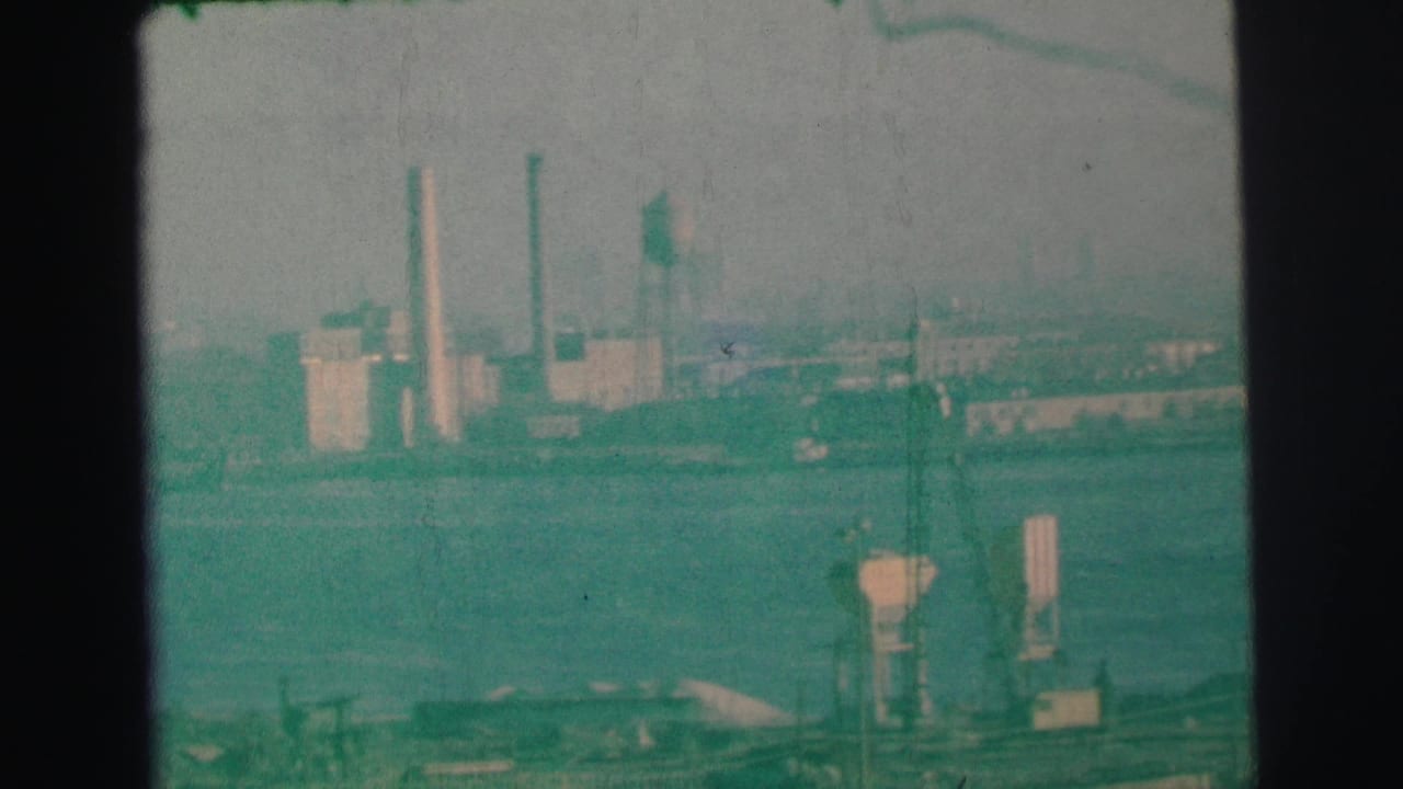 Distant factory complex with smokestacks and water tower beyond a hazy waterway.
