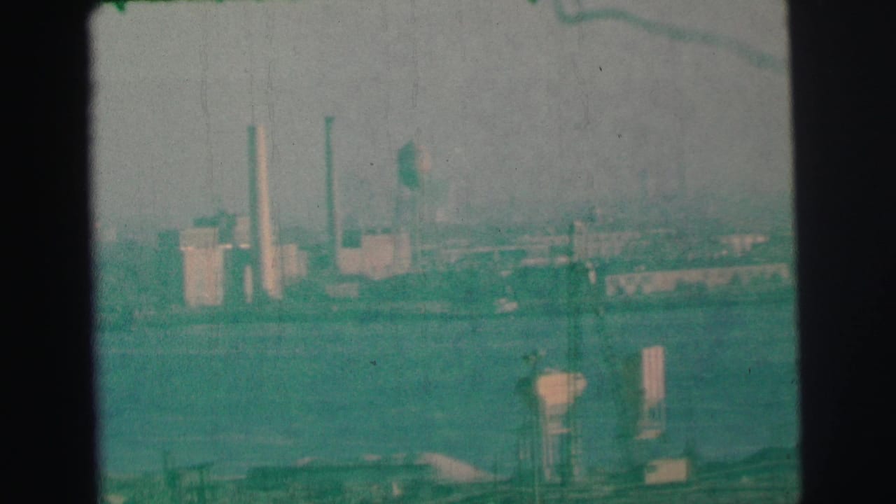 Industrial shoreline with smokestacks, water tower, and soft haze over water.