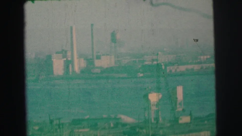 Green-tinted 8mm view of a 1973 industrial waterfront near Lynbrook, with low buildings, smokestacks, and visible film wear.