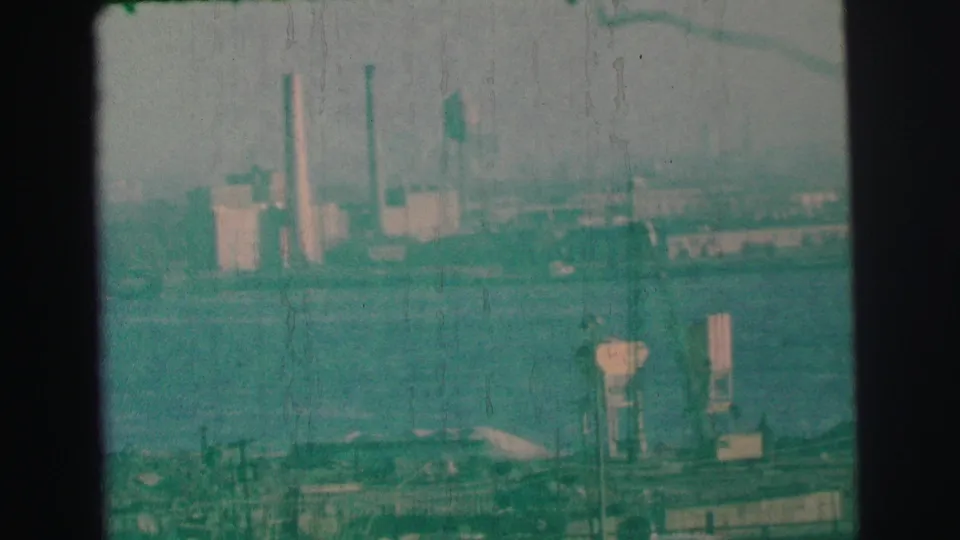 Soft-focus Lynbrook-area waterfront view from 1973, with distant smokestacks, low industrial buildings, and haze.