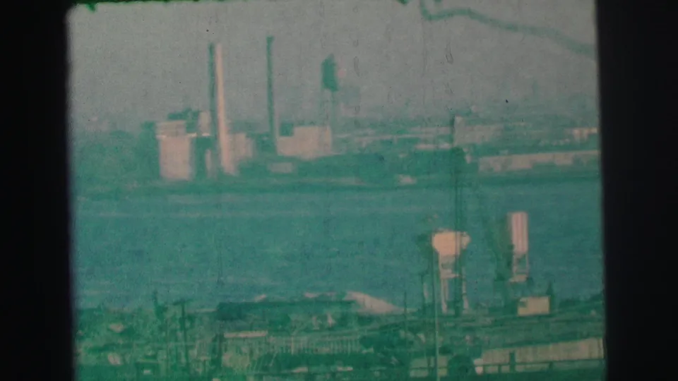 Green-tinted 1973 home-movie frame near Lynbrook showing water, an industrial shoreline, smokestacks, and foreground structures.