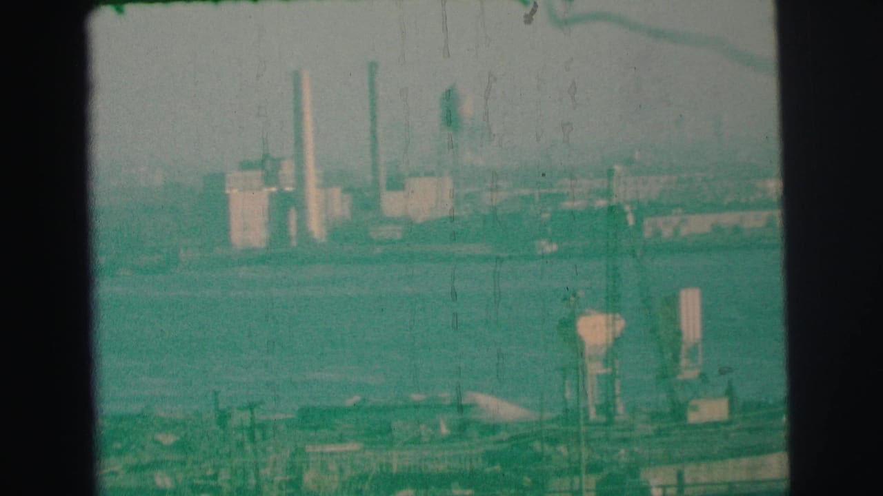 Hazy shoreline with smokestacks, towers, and industrial buildings.