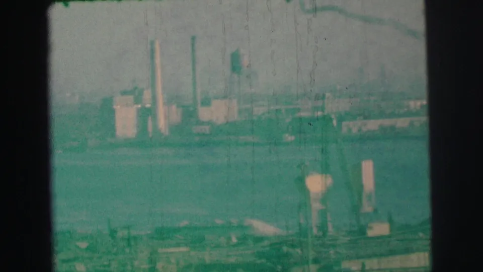 1973 Lynbrook, New York 8mm still showing a blurred industrial waterfront, tall stacks, cranes or towers, and water in the foreground.