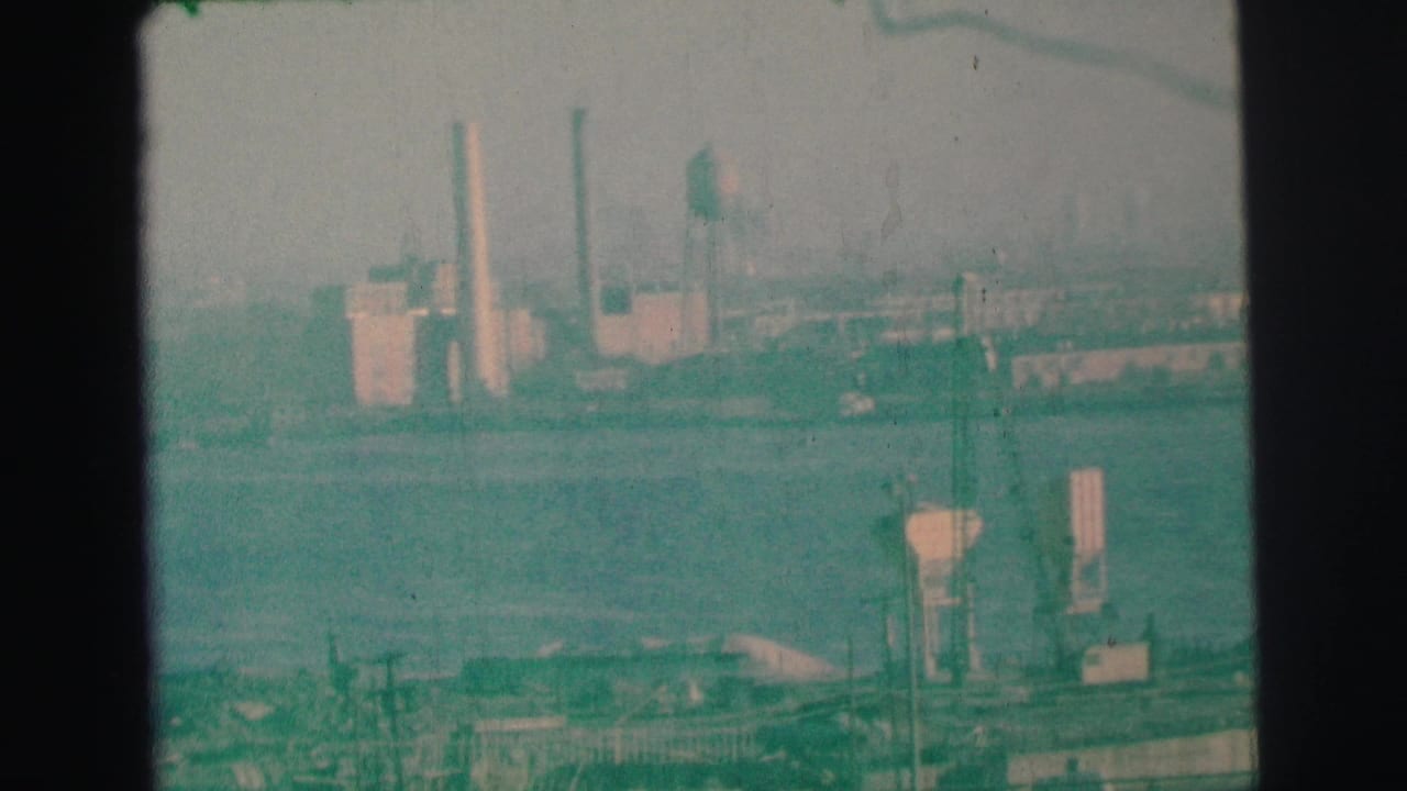 Green-tinted 1973 8mm footage in Lynbrook shows lake water, shoreline structures, and distant buildings under a hazy sky.