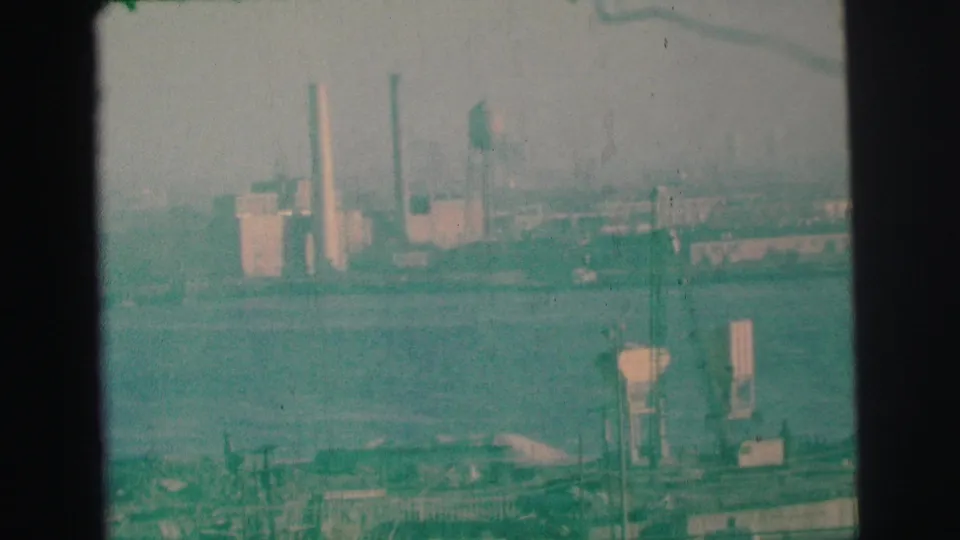 Green-tinted 1973 8mm footage in Lynbrook shows lake water, shoreline structures, and distant buildings under a hazy sky.