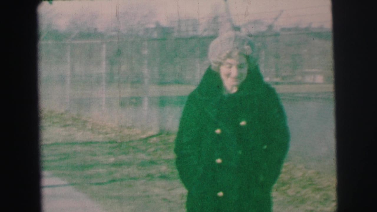 Woman in winter clothing looks toward the camera in a yard.