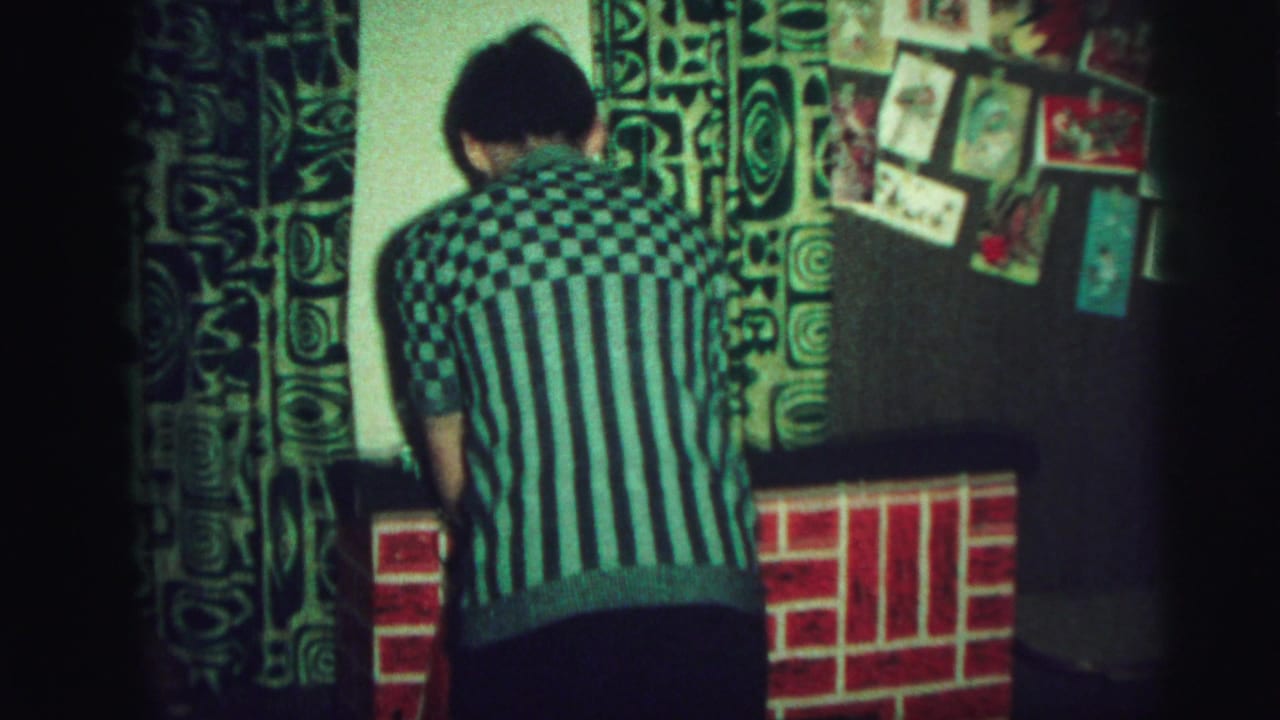 Teen in a green striped sweater stands with back to camera near the fake fireplace.