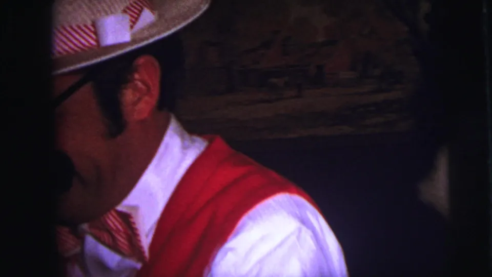 The Lynbrook 1973 home movie shows the costumed man turning in profile, with his red vest, bow tie, hat, and glasses visible in low light.