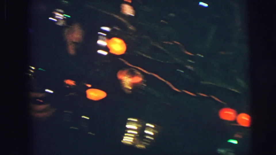Close 1973 Lynbrook holiday frame showing dark tree branches, glowing ornaments, and small points of light.