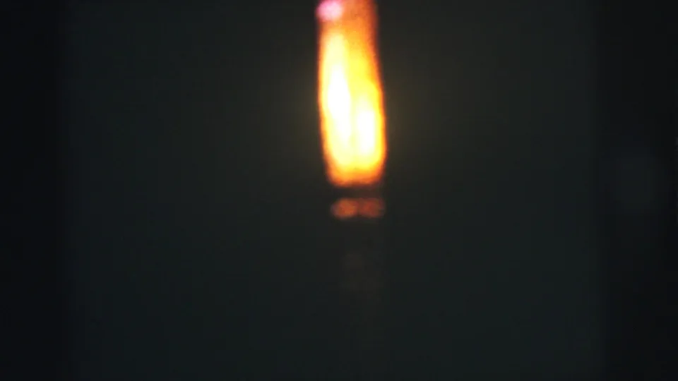 A soft, bright flame burns in darkness in 1973 Lynbrook, New York 8mm home-movie footage.