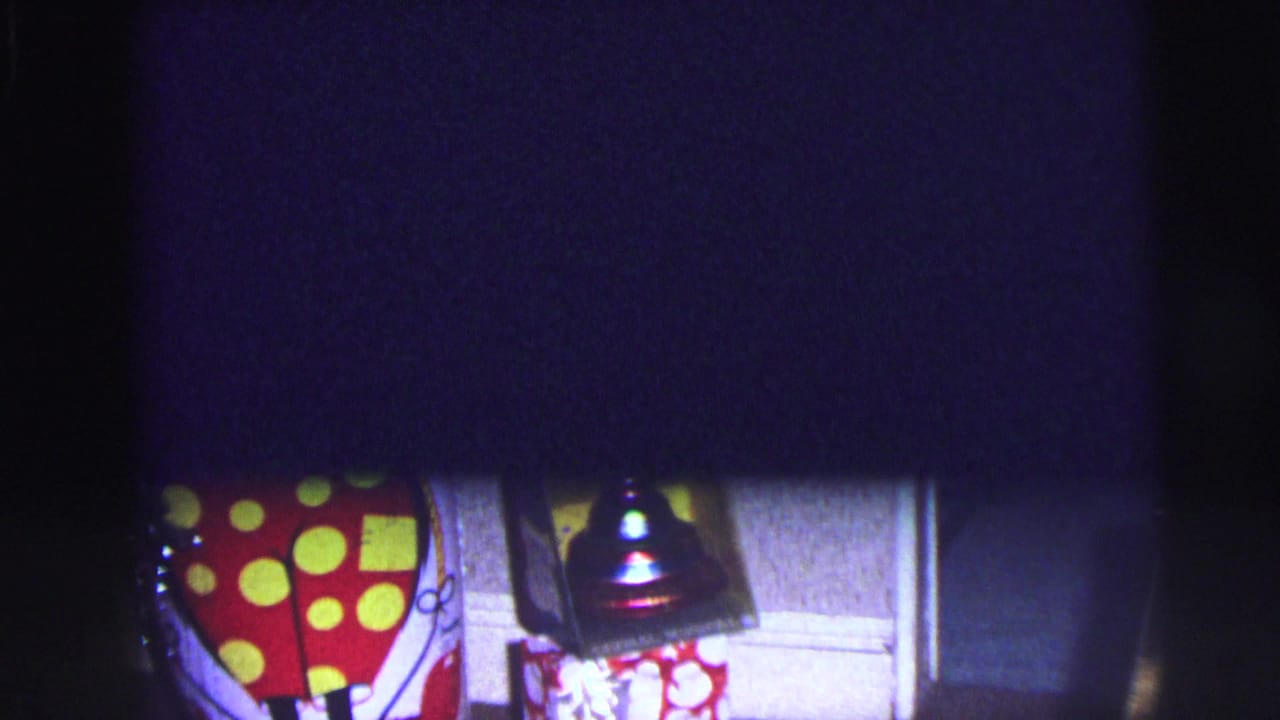 Dark interior frame with partial clown cutout, small boxed bell, and wall paneling.