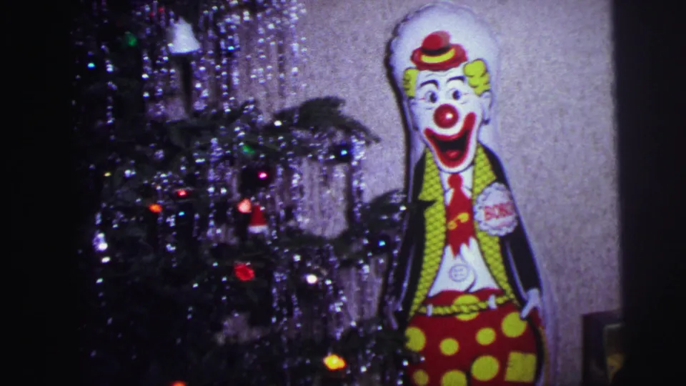 1973 Lynbrook home-movie frame with tinsel, tree lights, and a Bobo the Clown cutout near the holiday display.