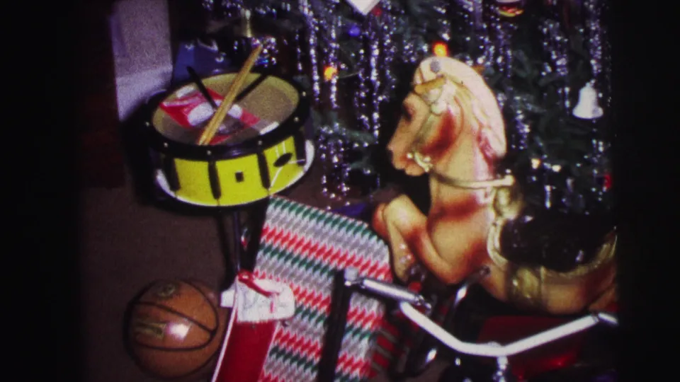 1973 Lynbrook home interior showing a yellow toy drum, rocking horse, basketball, wrapped presents, and tricycle handlebars near the Christmas tree.