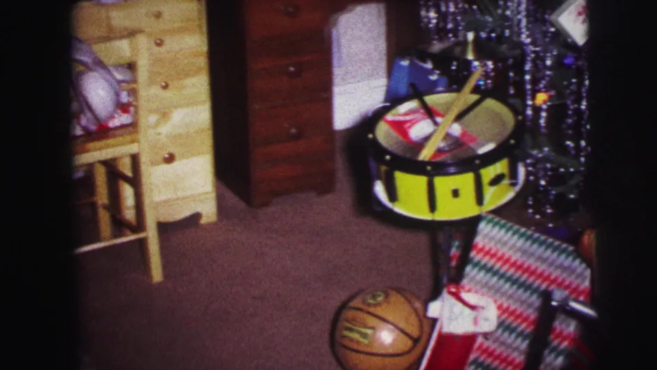 1973 Lynbrook frame showing a toy drum, basketball, wrapped present, tricycle handlebar edge, tinsel tree, and wood furniture in a private room.