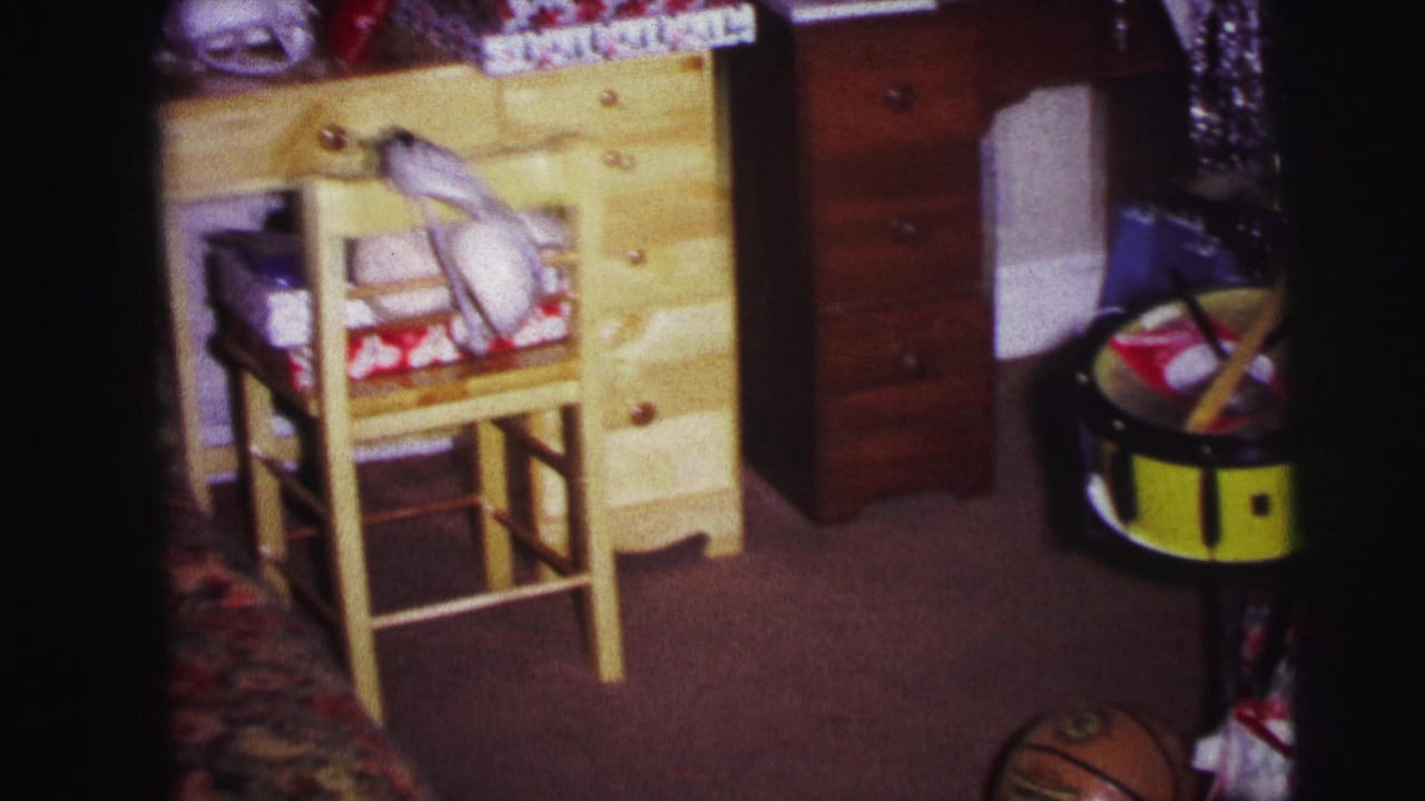1973 Lynbrook home-movie frame of a child's bedroom with a wooden desk, chair, wrapped gifts, sports gear, toy drum, and basketball.
