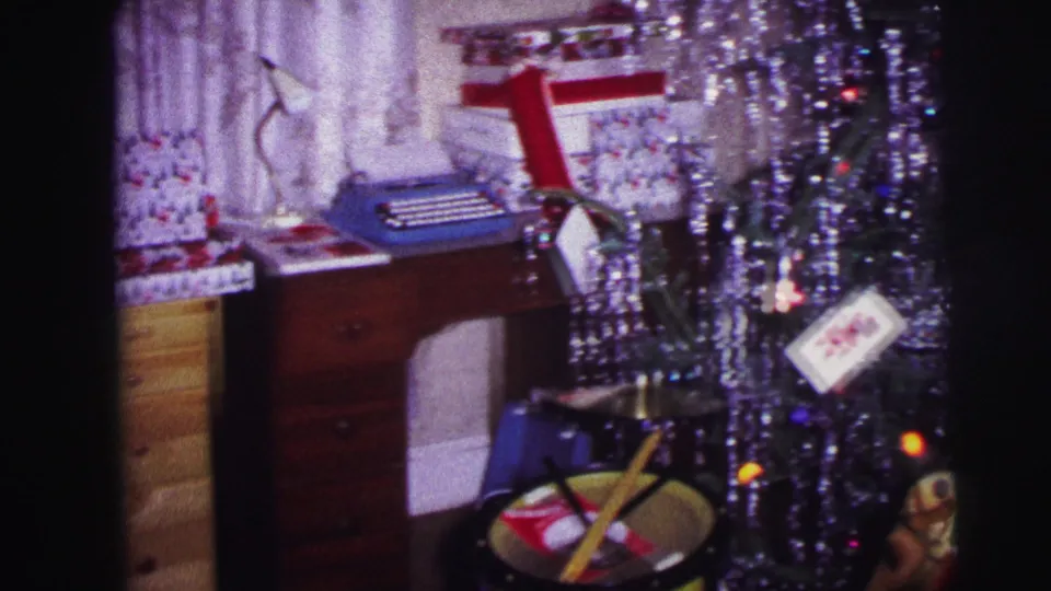 1973 Lynbrook holiday interior with a blue typewriter, wrapped gifts, hanging tinsel, toy drum, and the edge of a Christmas tree.
