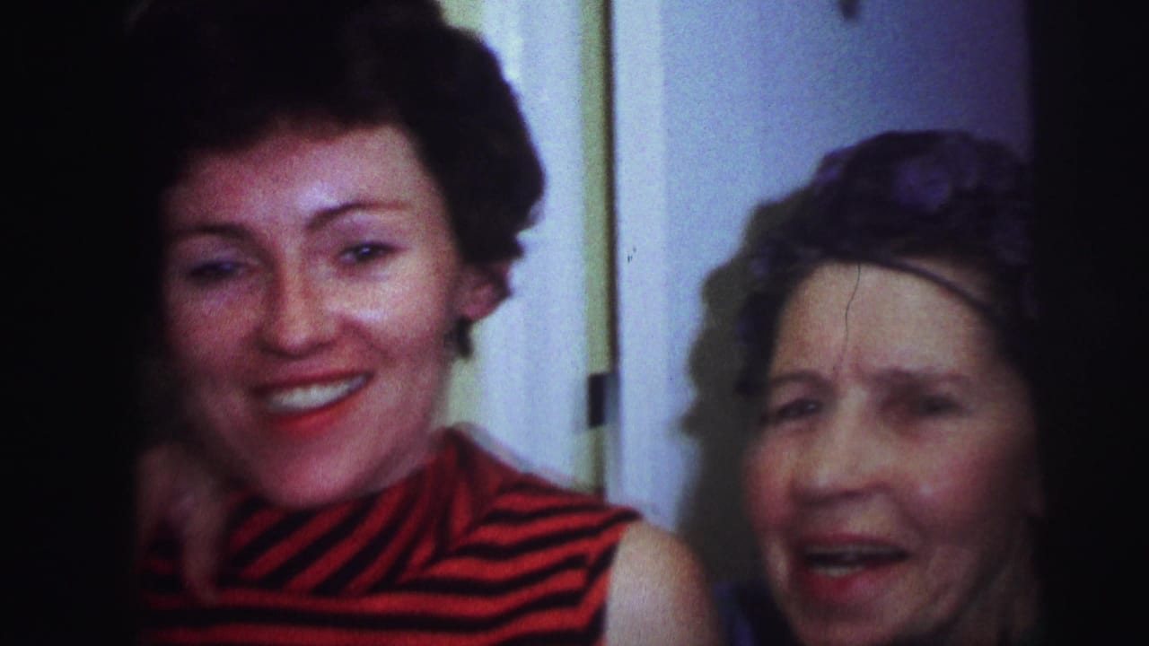 1973 Lynbrook home-movie frame of two adult women close together indoors, one smiling toward camera beside an older woman in hair rollers.